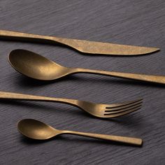 three golden forks and two spoons on a table with a black surface in the background