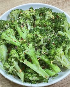 a white bowl filled with broccoli on top of a wooden table and topped with sesame seeds