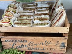 a wooden box filled with sandwiches on top of a table next to other food items