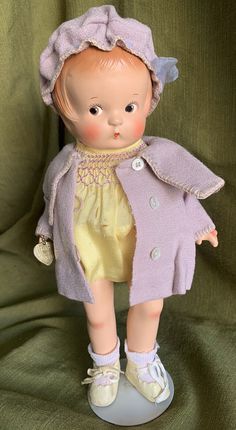 a small doll is wearing a purple coat and yellow dress with white shoes on it