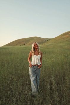 a woman standing in tall grass with her hands on her hips