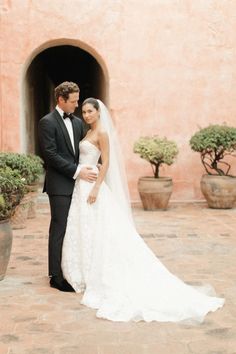 a bride and groom standing in front of a pink stucco building with potted plants