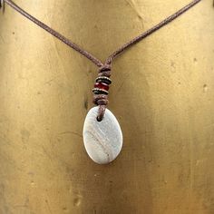 Beach pebble necklace, beige striped raw stone pendant, rock jewellery, brown cotton cord, beach found rock to wear I found this pebble on the beach in Cornwall and hung it on a brown cotton cord. The pebble is beige colour and has a faint stripes running through it I have drilled the pebble and hung it on a knotted adjustable natural coloured cotton cord  with a narrow red glass bead and two narrow bronze beads  The pebble measures approximately 27mm tall, 19mm wide and 5mm thick, the over all Brown Pendant Jewelry For Beach, Brown Pendant Jewelry For The Beach, Minimalist Waxed Cord Jewelry For Beach, Brown Waxed Cord Beach Necklaces, Brown Waxed Cord Necklaces For The Beach, Beach Necklaces With Brown Natural Stones, Beach Necklace With Brown Natural Stones, Beach Brown Necklace With Natural Stones, Handmade Cord Jewelry For The Beach