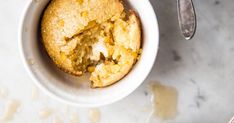 a muffin in a white bowl next to a spoon on a marble counter top