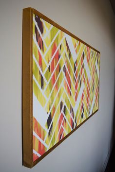 a painting hanging on the wall next to a wooden framed artwork piece with an orange, yellow and red geometric design