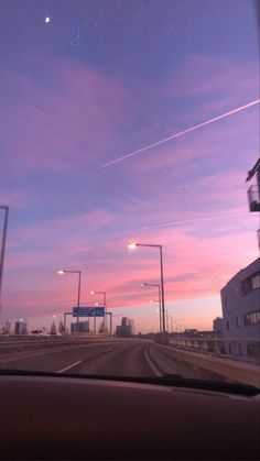 the sun is setting behind some buildings and street lights as seen from inside a car