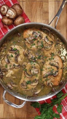 a pan filled with meat and mushrooms on top of a wooden table next to some parsley