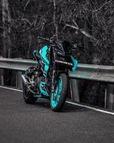 a blue and black motorcycle parked on the side of a road next to some trees