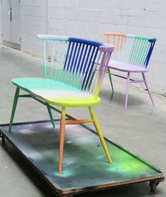 three colorful chairs sitting on top of a metal cart in front of a white brick wall