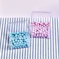 two clear boxes filled with pink and blue candies on a striped tablecloth surface