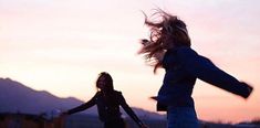 two women are playing with a frisbee at sunset