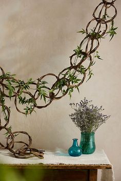 a table topped with a vase filled with flowers and vines next to a sculpture made out of branches