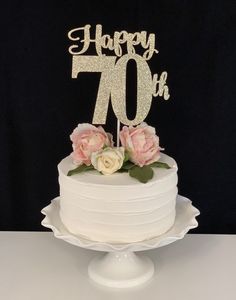 a white cake with pink flowers and the number seventy on top is sitting on a table