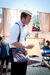 a man wearing a hat and suspenders is standing in front of some people at an outdoor event