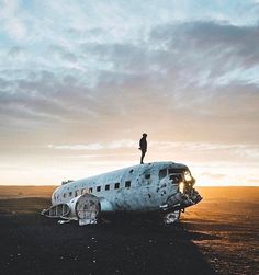 a man standing on top of an airplane in the middle of nowhere at sunset or dawn