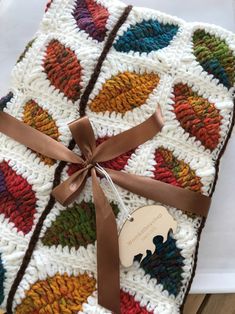 a crocheted blanket with a brown ribbon tied around it and a tag on top