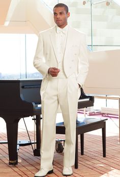 a man in a white suit standing next to a piano