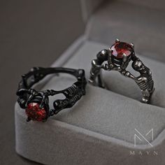 two rings with red stones are sitting in a box on top of a gray surface