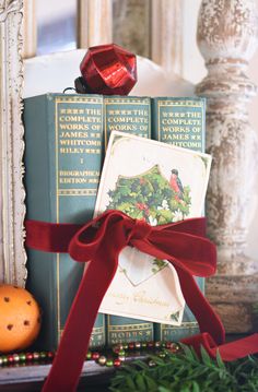 a stack of christmas books with a red ribbon tied around it and an orange on top