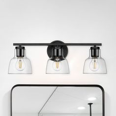 three light bathroom vanity fixture with clear glass shades and black metal frame, on white wall