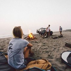 two people sitting on the beach next to a campfire