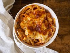 a white bowl filled with pasta on top of a wooden table next to a napkin