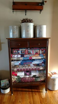 an old dresser is covered with quilts and buckets on it's shelf