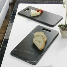 two cutting boards with slices of bread on them sitting on a table next to a potted plant