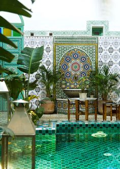 an outdoor pool surrounded by potted plants next to a wall with tiles on it