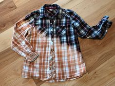 an orange and black plaid shirt laying on top of a wooden floor next to a pair of jeans