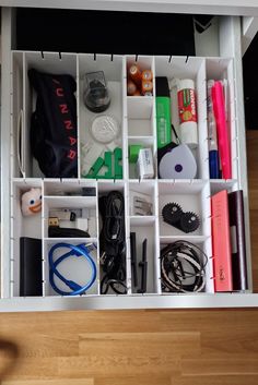 an organized drawer with various items in it on top of a wooden floor next to a lamp