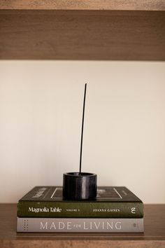 a stack of books sitting on top of a wooden shelf next to a black candle