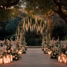 an outdoor wedding setup with candles and flowers on the aisle, surrounded by greenery