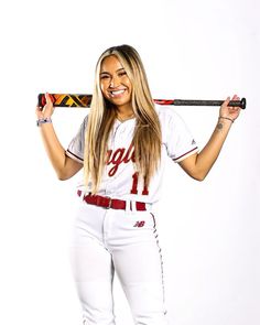 a beautiful young lady holding a baseball bat over her shoulder and smiling at the camera