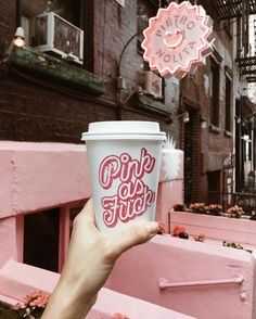 someone holding up a pink cup with the word pink out on it in front of some buildings