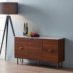 a wine bottle and two glasses on a wooden cabinet next to a floor lamp in a room