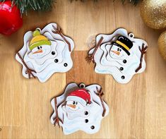 three snowmen with hats and scarfs sitting on top of a wooden table next to christmas decorations