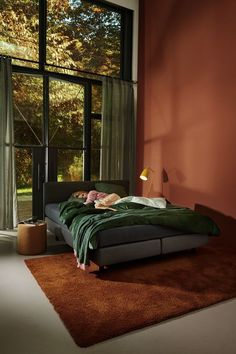 a bedroom with a large window and a bed in front of an orange wall that has a green blanket on it