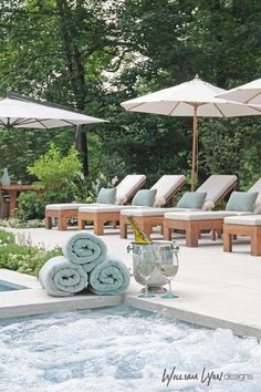 an outdoor hot tub with towels and wine glasses on the edge, surrounded by lounge chairs