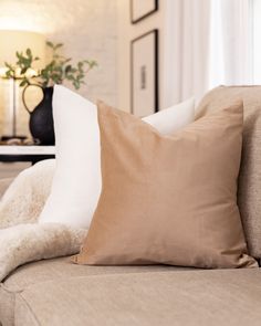 a couch with two pillows on it in front of a table and vase filled with flowers