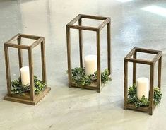 three wooden lanterns with candles and greenery in them on the floor, one is empty