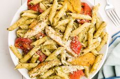 a white plate topped with pasta covered in pesto and tomato sauce next to a fork