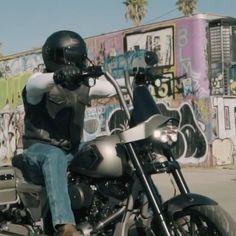 a man riding on the back of a motorcycle down a street next to graffiti covered walls