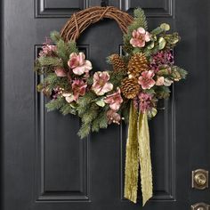 a wreath with flowers and pine cones hangs on the front door's black door