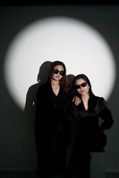 two women standing next to each other in front of a white wall with a shadow on it