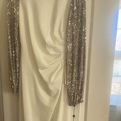 a white dress with silver sequins hanging from it's hanger in front of a window