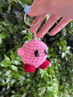 a hand holding a pink crocheted keychain with black eyes and nose