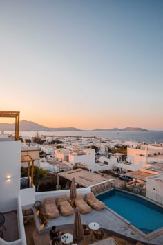 an outdoor swimming pool with lounge chairs and umbrellas in front of the ocean at sunset