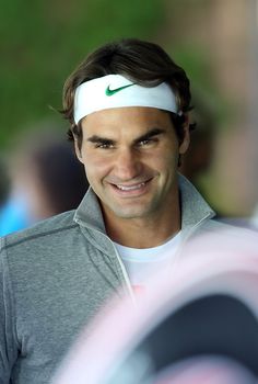 a man with a tennis racket in his hand and wearing a headband smiles at the camera