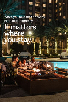 a group of people sitting around a fire pit in front of a building at night